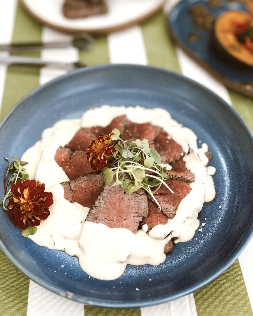 Carne fatiada ao creme com flores comestíveis e brotos