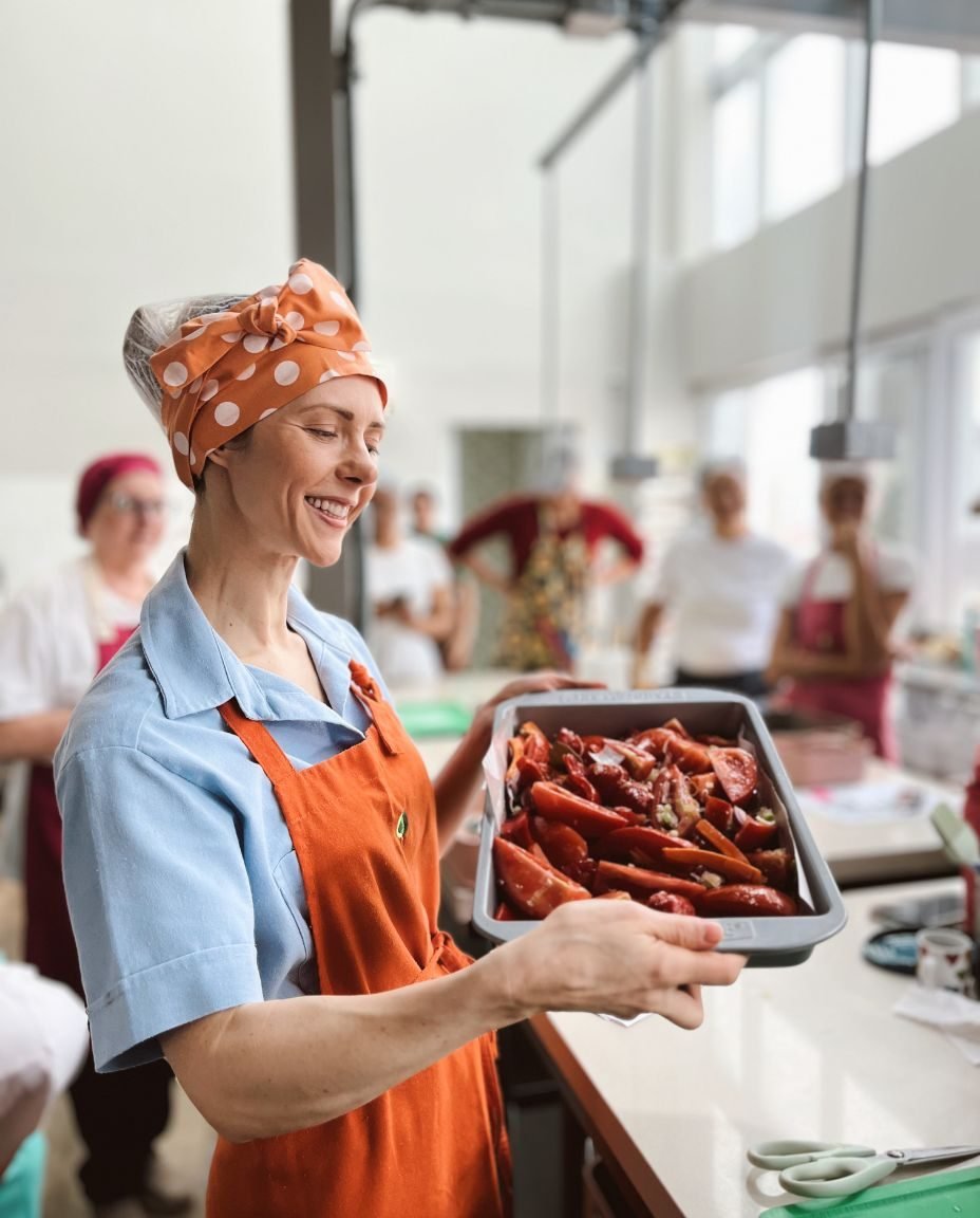 Fran de avental laranja segurando uma travessa de legumes na cozinha